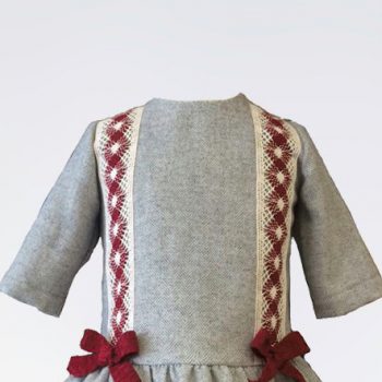 Detalle delantero del vestido de niña en tono gris con tira bordada en rojo y beige